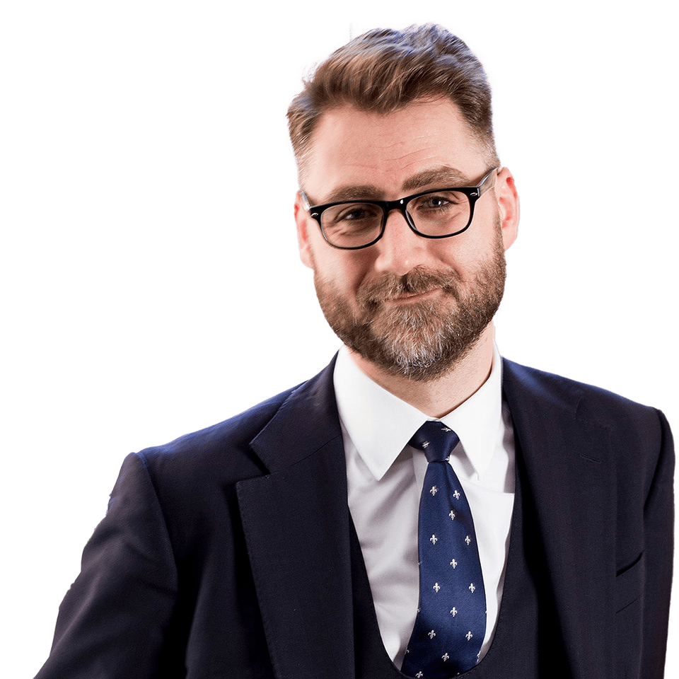 A man with glasses, a beard, and wearing a suit and tie is smiling while looking at the camera.